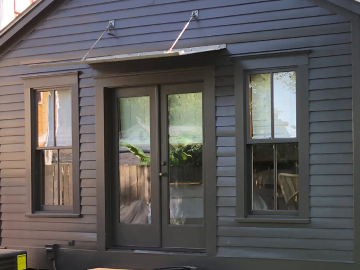 Detail of a Houston exterior remodel: new French doors under a small metal awning, with black lap siding and the window trim beside them