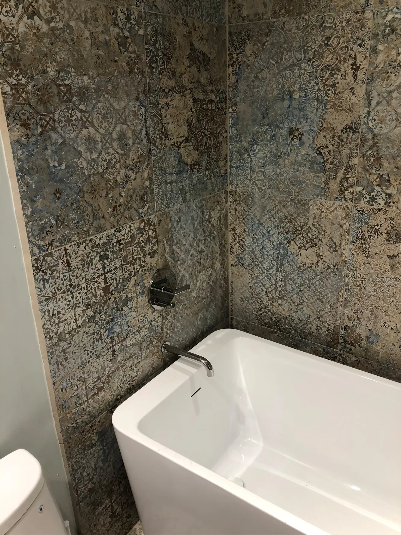 Freestanding tub against patterned tile walls with a wall-mounted tub filler in a remodeled Houston bathroom