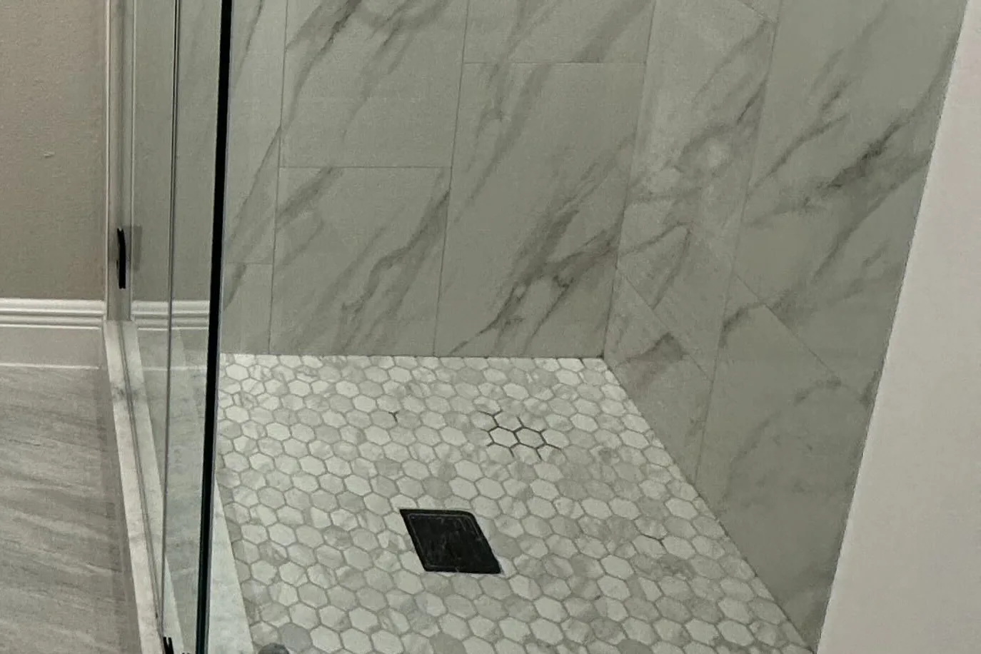 Hexagon mosaic shower floor, square drain and marble-look wall tile behind a frameless glass panel in a remodeled Houston bathroom